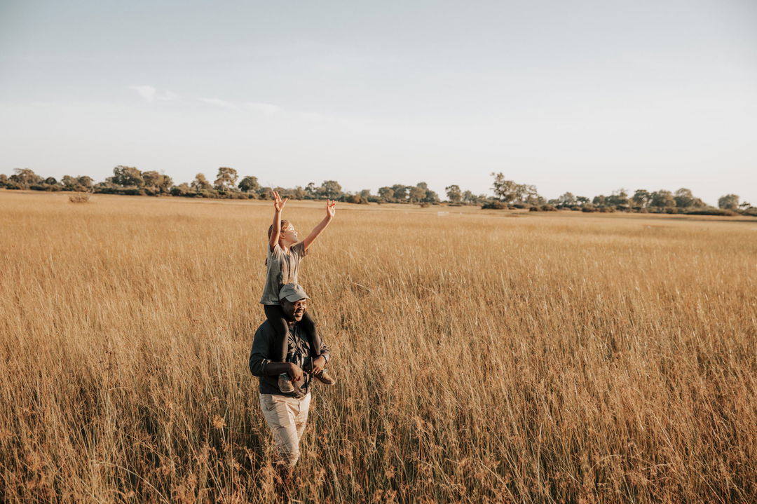 guide walking with boy on his shoulders at Vumbura Plains Camp Wilderness Okavango Delta