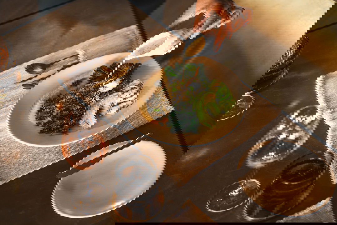 waiter pouring sauce over gourmet food served on table with wine at Wilderness Mombo Camp