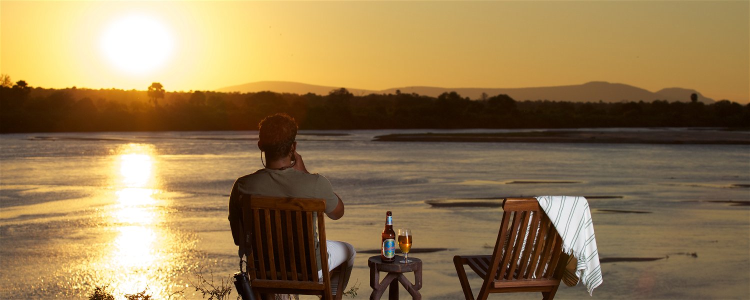 A man sitting on the side of The Rufiji River drinking a beer